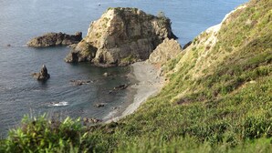 Un paysage côtier caractérisé par des falaises rocheuses, une plage de sable et une colline couverte d’herbe.