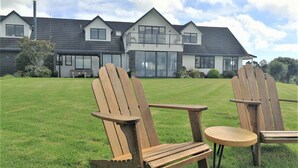 Une maison avec une grande pelouse, deux fauteuils Adirondack en bois et une petite table ronde.
