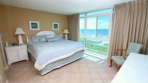 Habitación de hotel con una cama grande, una mesita de noche, una silla y vista al océano.
