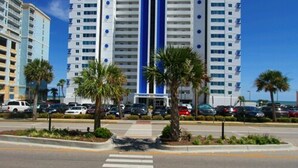 Un hotel de varios pisos con una banda vertical azul en el centro, rodeado de palmeras y coches aparcados.