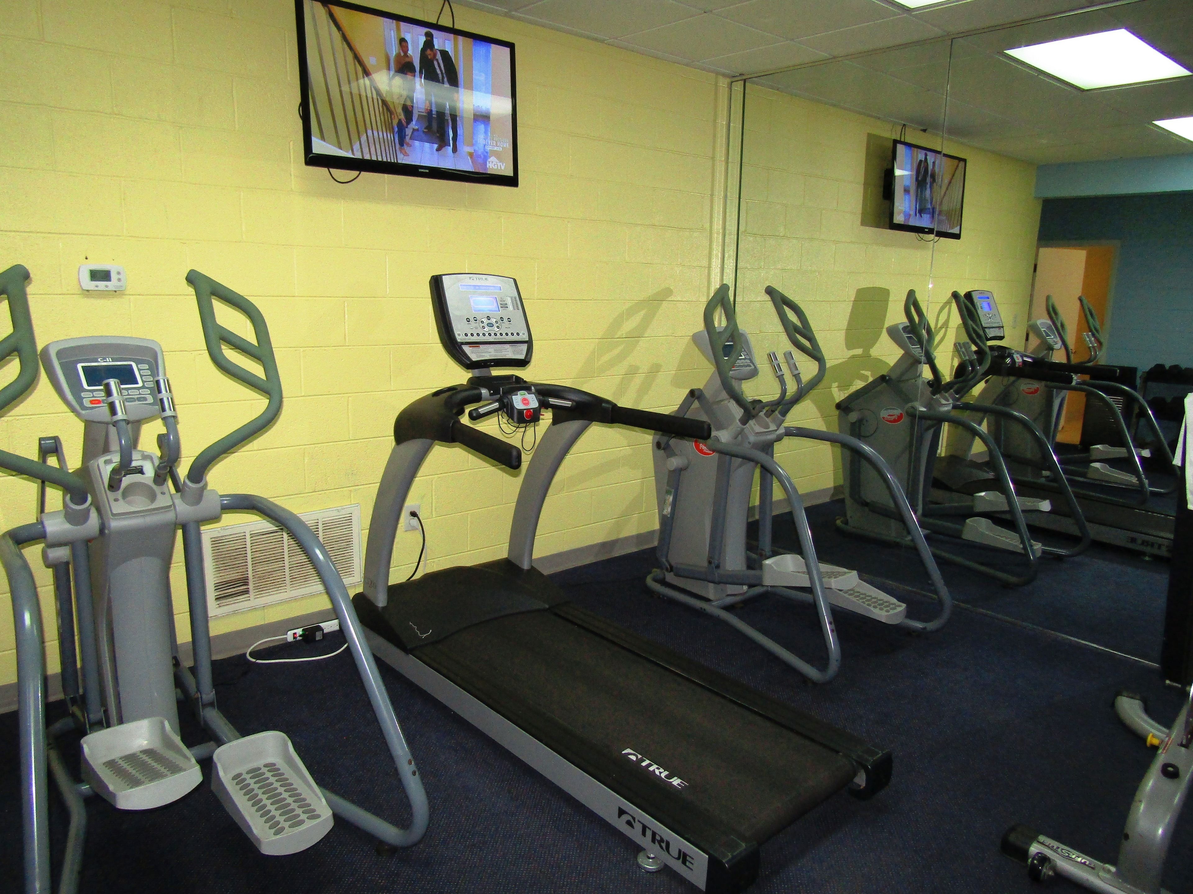 Une salle de sport équipée de tapis de course, de vélos elliptiques et d’un écran de télévision diffusant une vidéo d’entraînement.