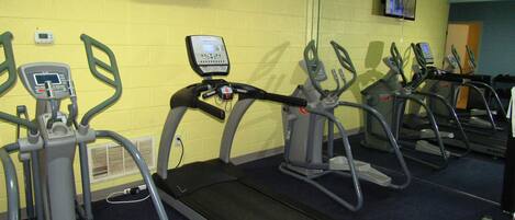 Une salle de sport équipée de tapis de course, de vélos elliptiques et d’un écran de télévision diffusant une vidéo d’entraînement.