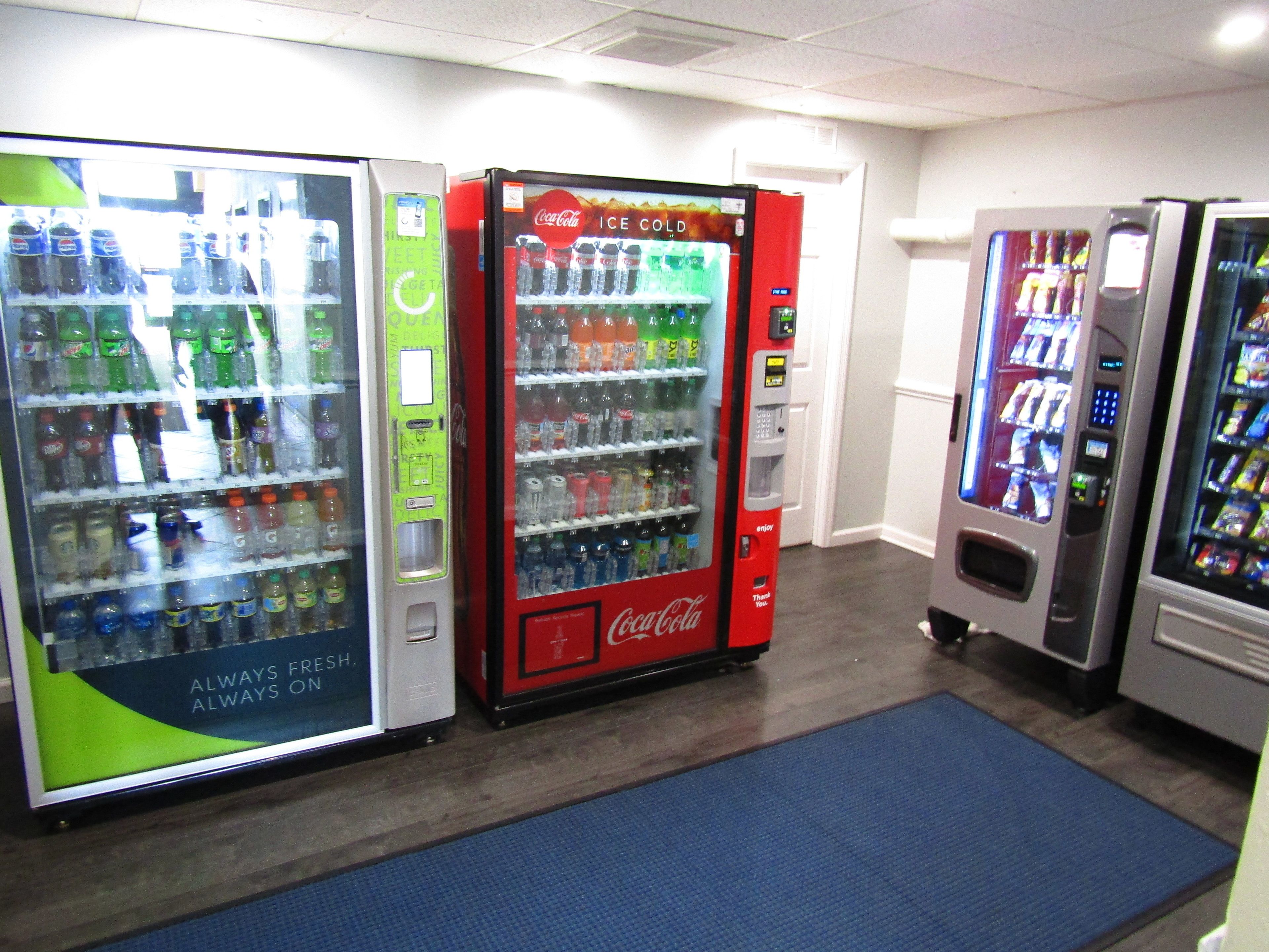 A row of vending machines in a hallway, including a Coca-Cola Ice Cold machine and a Pepsi machine.