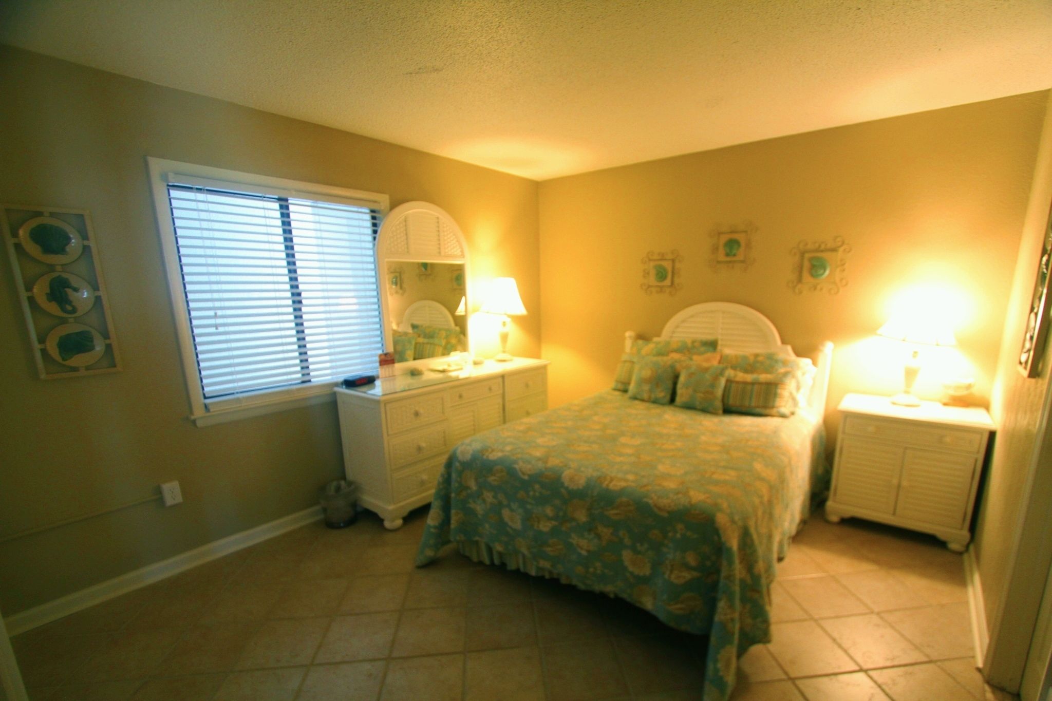 A bedroom with a bed, nightstands, a dresser, a window with blinds, and wall decorations.