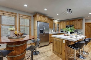 A kitchen with wooden cabinets, a stainless steel refrigerator, a bar area with stools, and a large island with bar stools. - Abode Mountainside, steps to ski lifts, hot tub, Old Town (Park City)