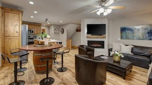 Une cuisine moderne avec des meubles en bois, un îlot central doté de tabourets de bar, un coin repas avec un canapé en cuir noir et une cheminée.