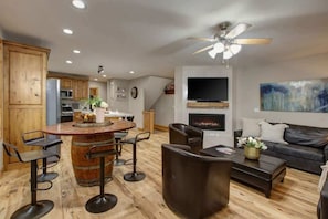 A modern kitchen with wooden cabinets, a central island with bar stools, a dining area with a black leather couch, and a fireplace. - Abode Mountainside, steps to ski lifts, hot tub, Old Town (Park City)