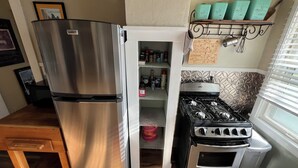 Ett kök med ett kylskåp i rostfritt stål, en inbyggd ugn och en spishäll. Ovanför spisen finns en hylla med behållare i turkos färg.