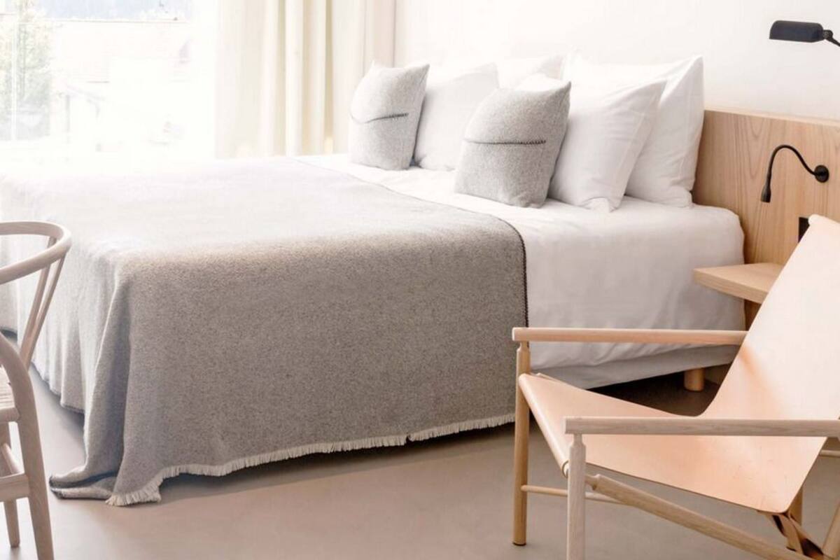 A bedroom with a bed, a desk, a chair, and a bedside table.
