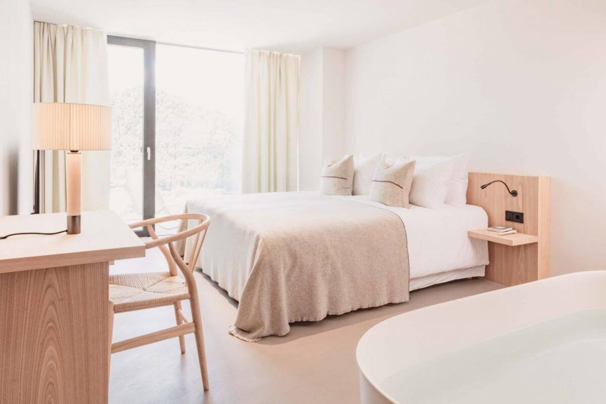 A modern hotel room with a large bed, a desk, a chair, and a bathtub.