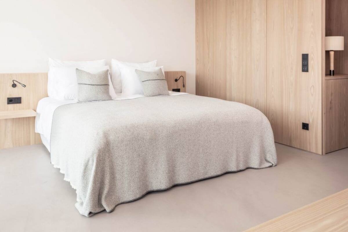 A modern bedroom with a large bed, wooden headboard, and a nightstand with a lamp.