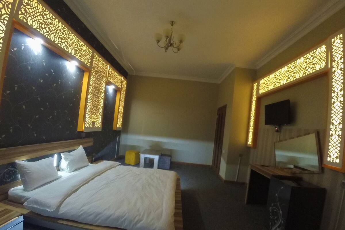 A hotel room with a bed, a TV, and decorative wall panels.