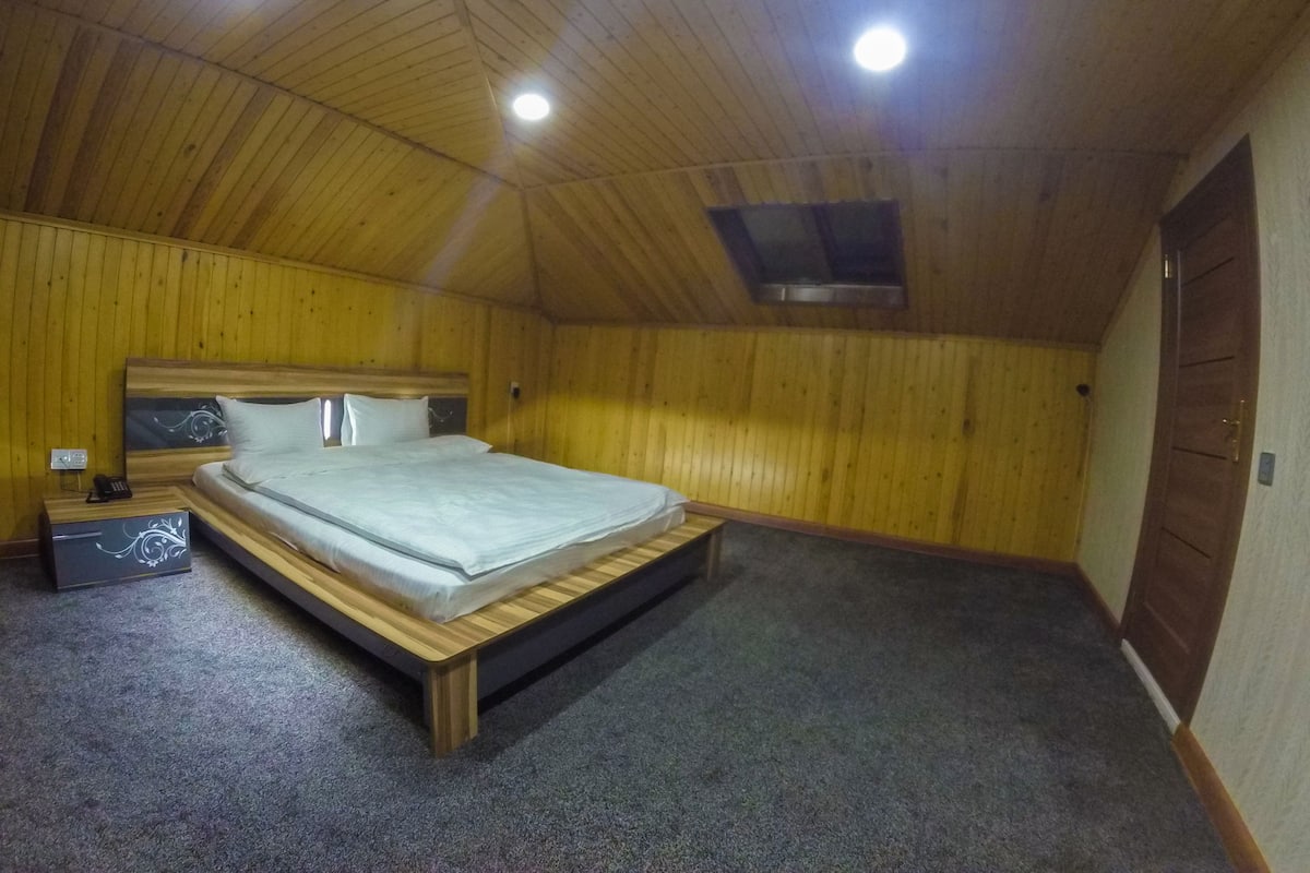 A bedroom with a wooden ceiling, a bed, a nightstand, and a wall-mounted heater.