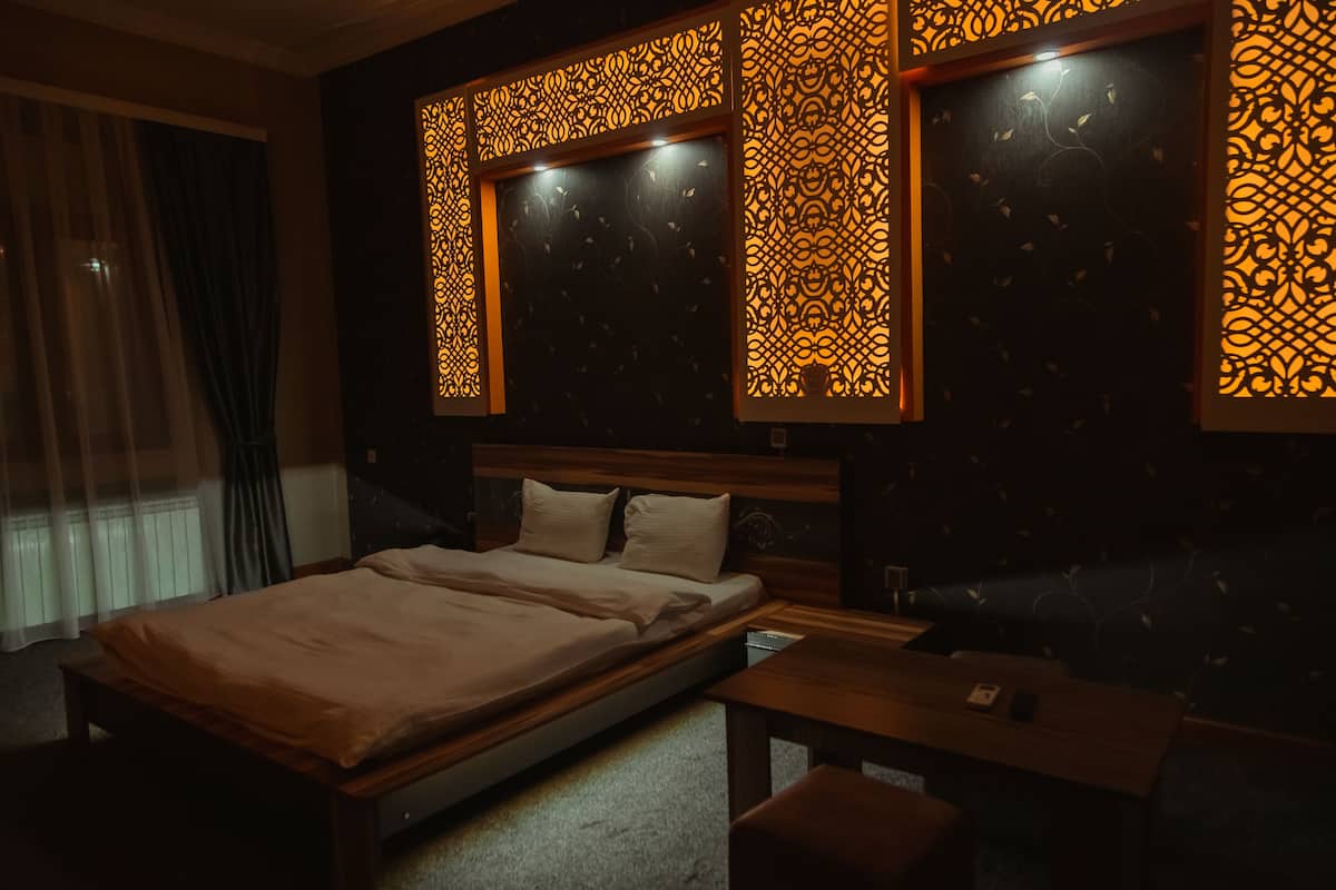A dimly lit bedroom with a bed, a bedside table, and a decorative wall panel.