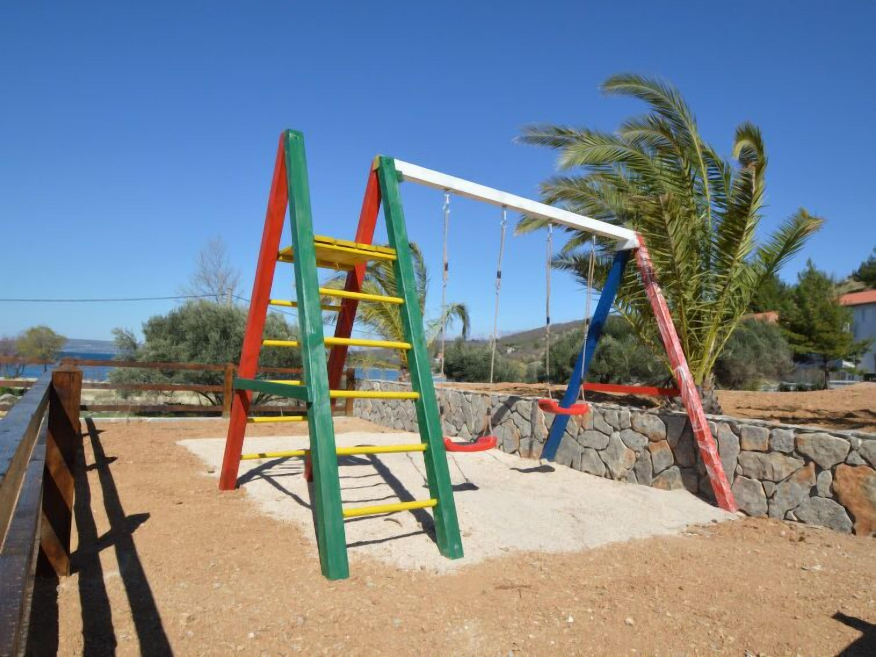 A playground with a ladder, swings, and a stone wall.