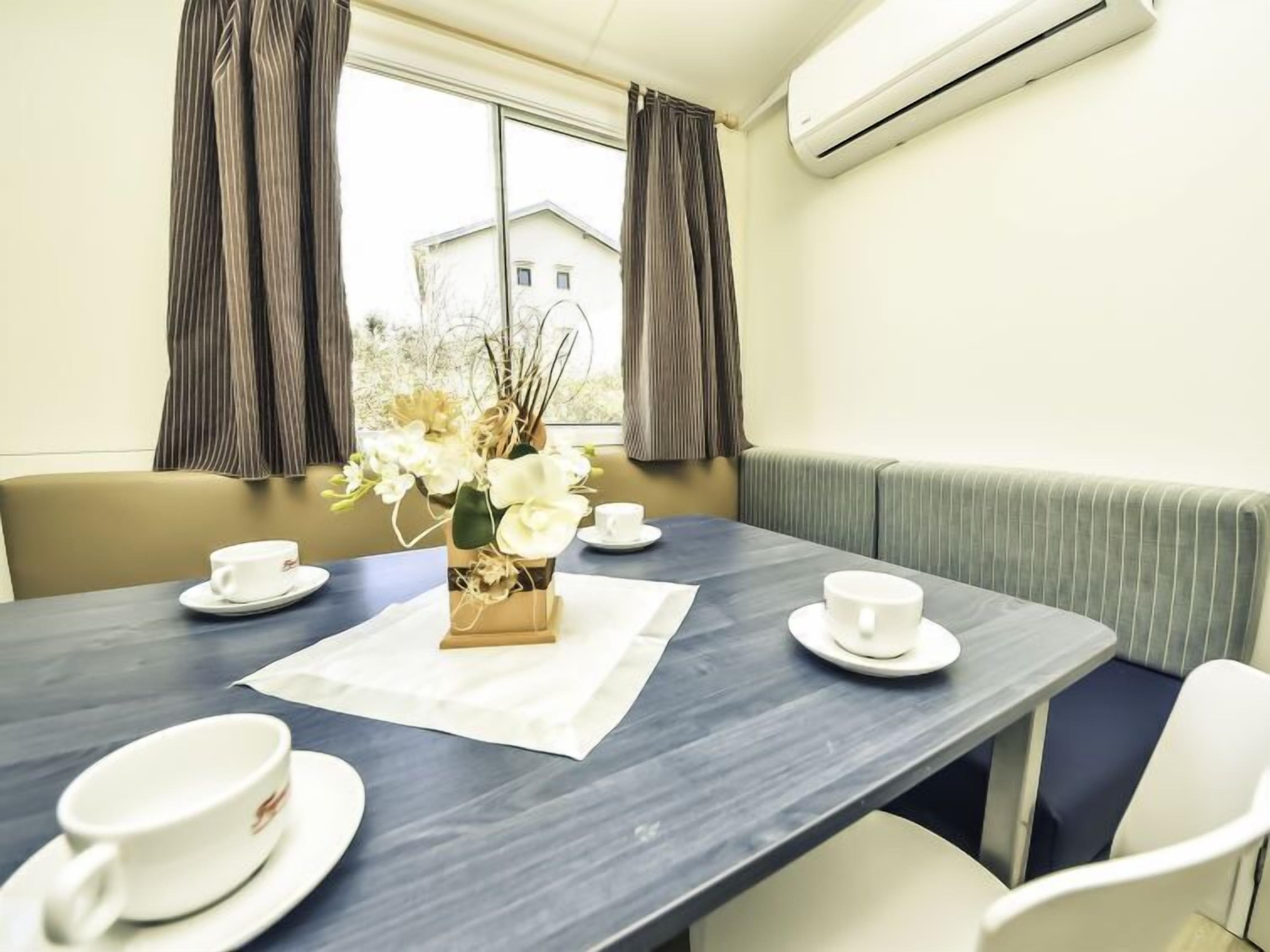 A dining area with a table set for two, a vase of flowers, and a view of buildings outside.