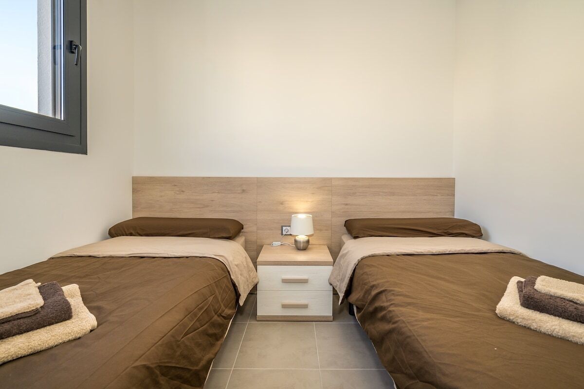 Une chambre double avec deux lits, une table de chevet avec une lampe et une fenêtre.