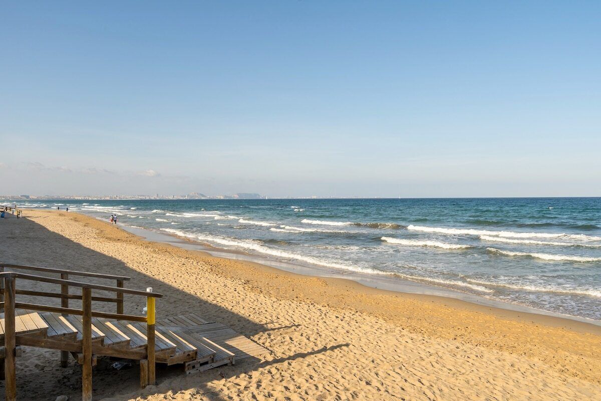 A beach with a wooden walkway leading to the water, sandy beach, and ocean waves.