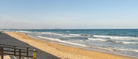 A beach with a wooden walkway leading to the water, sandy beach, and ocean waves.