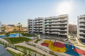 Ein moderner Wohnkomplex mit mehreren Balkonen, einem zentralen Innenhof mit Spielplatz und einem Schwimmbad.