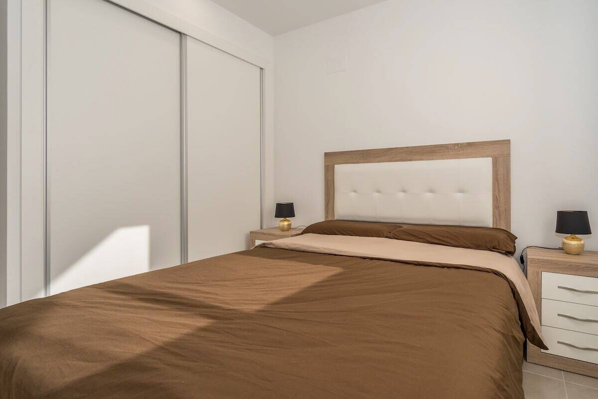 A bedroom with a bed, two bedside tables, a wooden headboard, and a sliding door.
