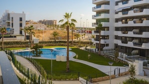 A modern hotel with a swimming pool, palm trees, and a view of the surrounding cityscape. - Apartamento Arenales (Arenales del Sol) (Arenales del Sol)