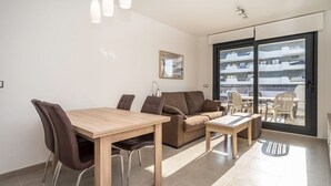 A modern living room with a wooden dining table, brown sofa, and a large sliding glass door leading to a balcony with outdoor furniture. - Apartamento Arenales (Arenales del Sol) (Arenales del Sol)
