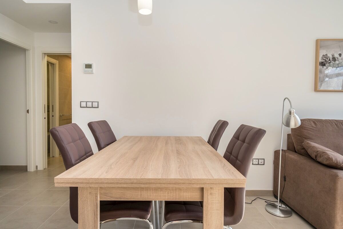 Een moderne eetruimte met een houten tafel, zes stoelen, een bank en een vloerlamp.