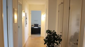 A hallway with a potted plant, doors, and a bed in the background. - Räddningsskolans lägenhetshotell (Skovde)