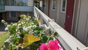A balcony with a flower planter and a red door. - Räddningsskolans lägenhetshotell (Skovde)