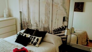 A bedroom with a bed, pillows, a bedside table, a lamp, a mirror, and a wall with a cityscape mural. - Precious century-old house recently restored, original stone and wooden beams (Segovia)