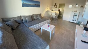 A modern living room with a grey sofa, a small white table, and a kitchen area in the background.