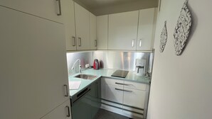 A compact kitchen with white cabinets, a stainless steel sink, a kettle, and a coffee maker.