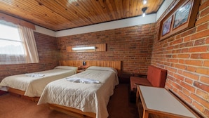 A room with two beds, a wooden table, and a brick wall. - Hotel del Campo (Quetzaltenango)