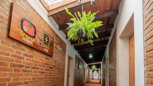 A hallway with brick walls, wooden ceiling beams, and a hanging plant. - Hotel del Campo (Quetzaltenango)