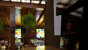 A restaurant with wooden tables and chairs, a high ceiling with hanging plants, and a stained glass window. - Hotel del Campo (Quetzaltenango)