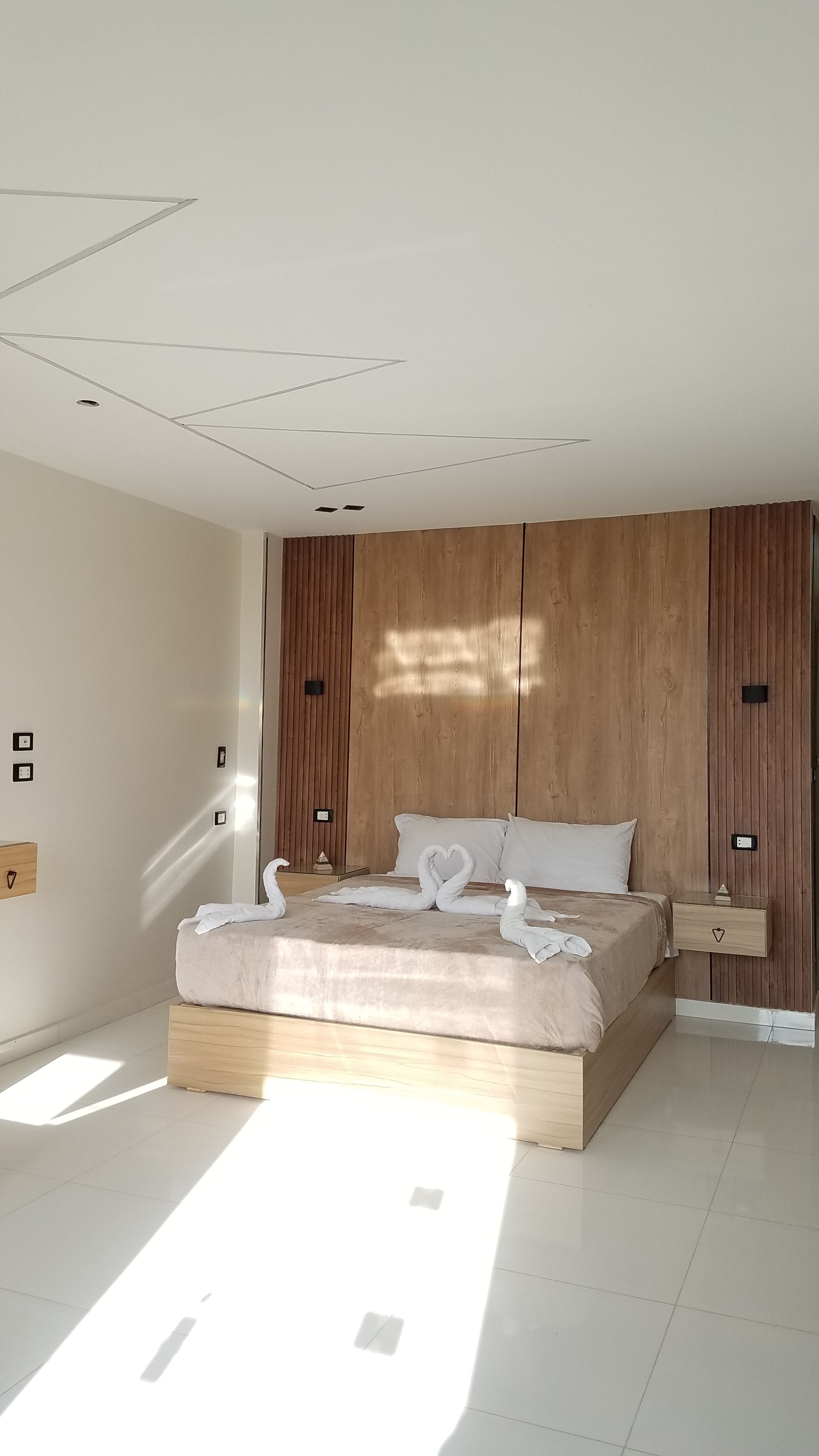 A modern bedroom with a large bed, wooden paneling on the walls, and a skylight.