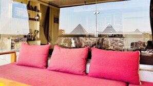 A bed with red pillows, a glass partition, and a view of pyramids. - Pyramids Terrace INN (Giza)