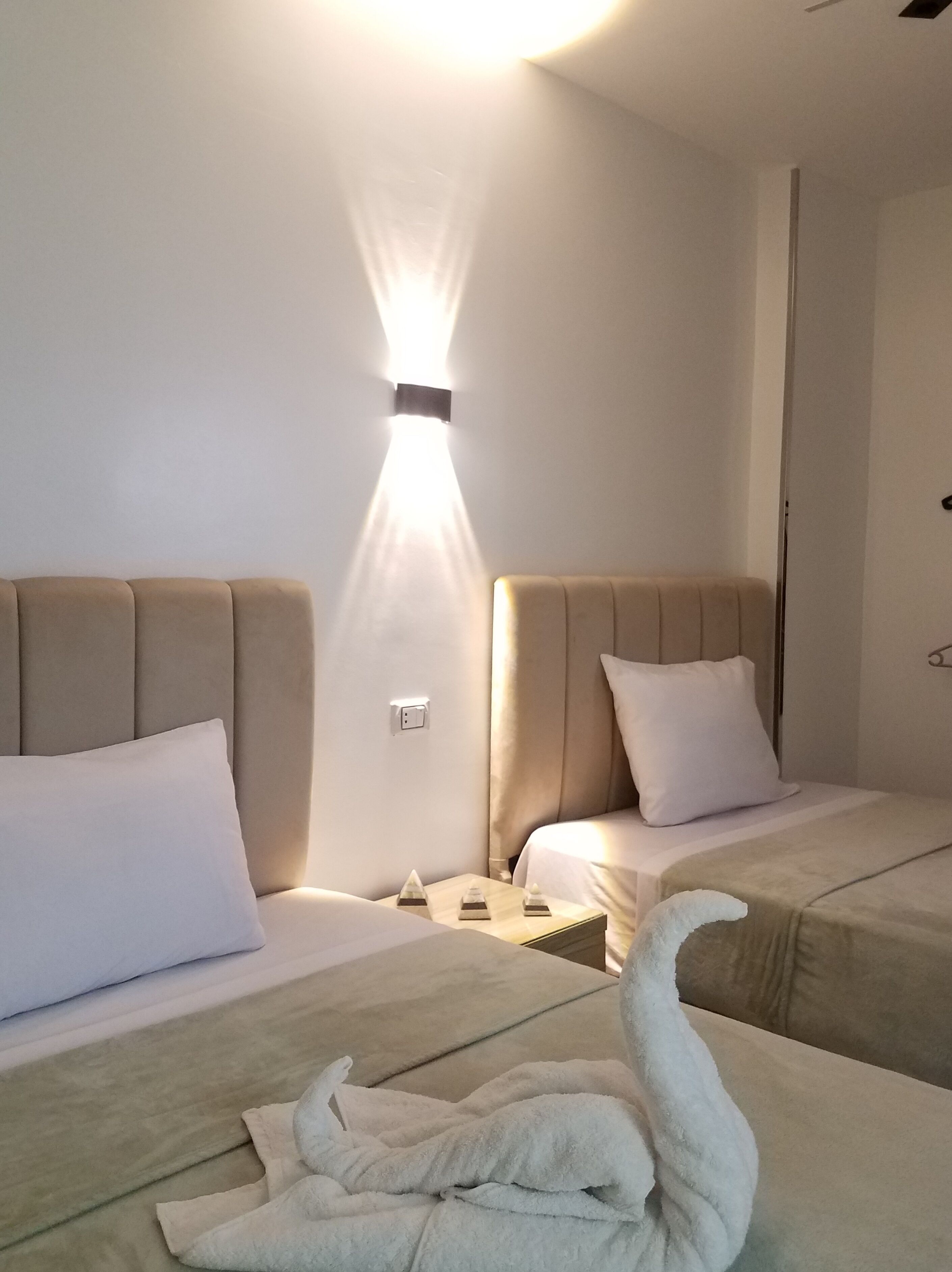 Ein Hotelzimmer mit zwei Betten, einem Nachttisch, einer Wandleuchte und einem schwanenförmigen Handtuch.