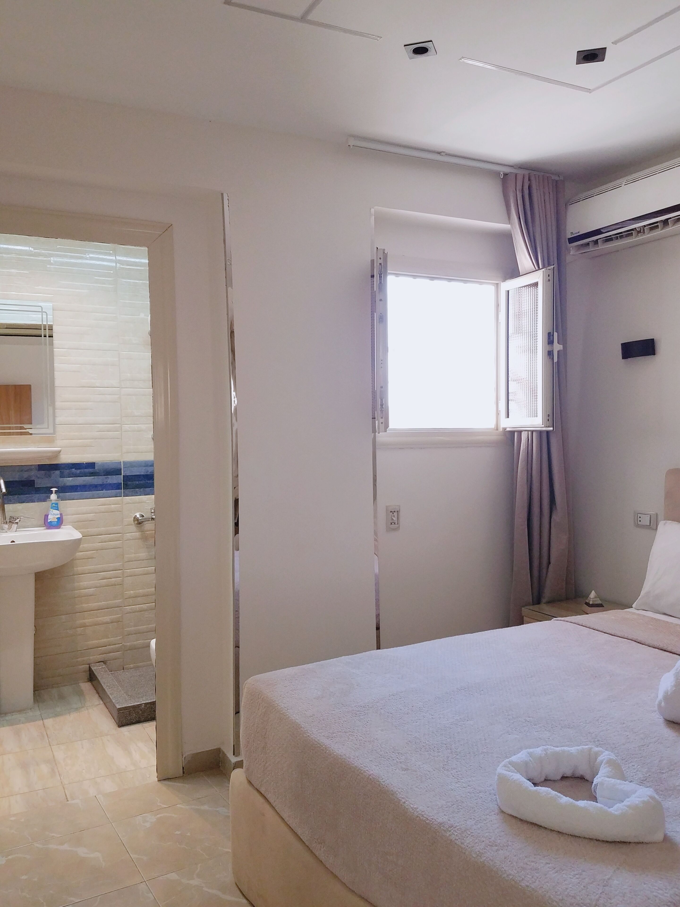 Ein Hotelzimmer mit Bett, Fenster, Badezimmer mit Waschbecken und Dusche.