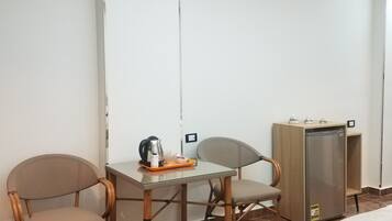 A room with a dining table, two chairs, a refrigerator, and a bed.