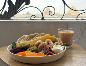 A bowl of assorted fruits and a glass of iced coffee on a balcony with a view of pyramids. - Pyramids Terrace INN (Giza)