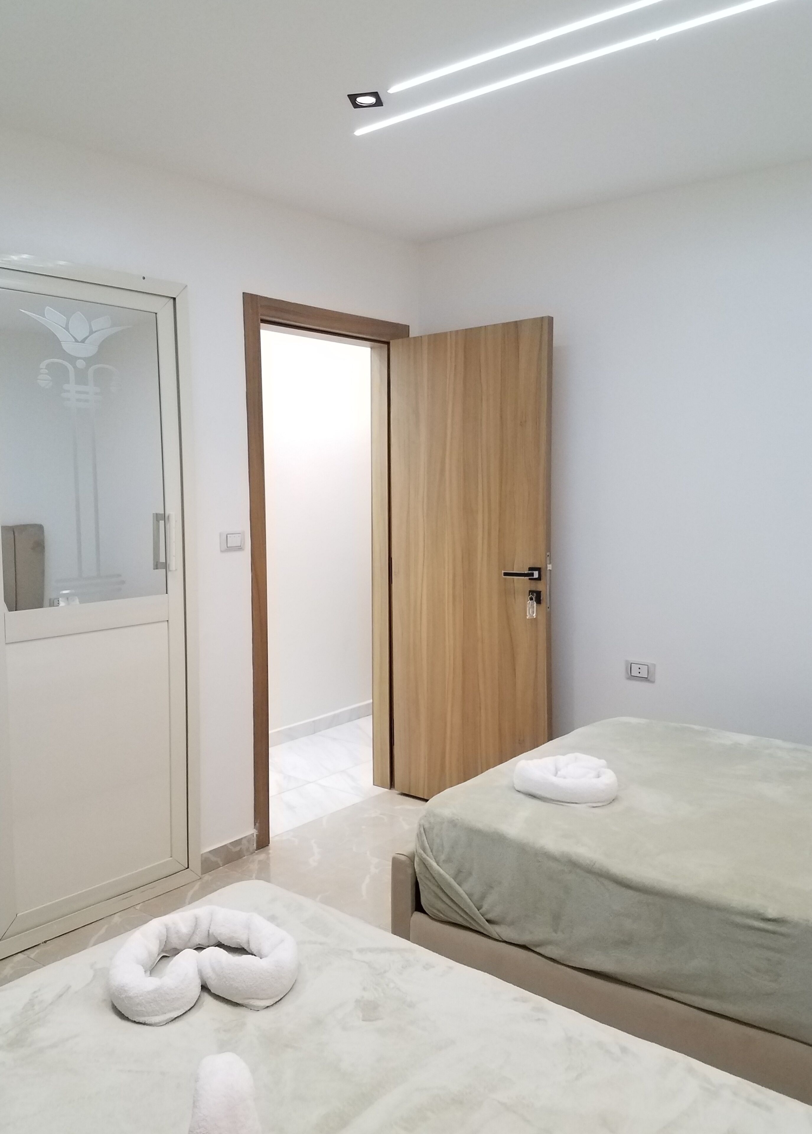 A hotel room with a bed, a wooden wardrobe, a mirror, and a door leading to another room.