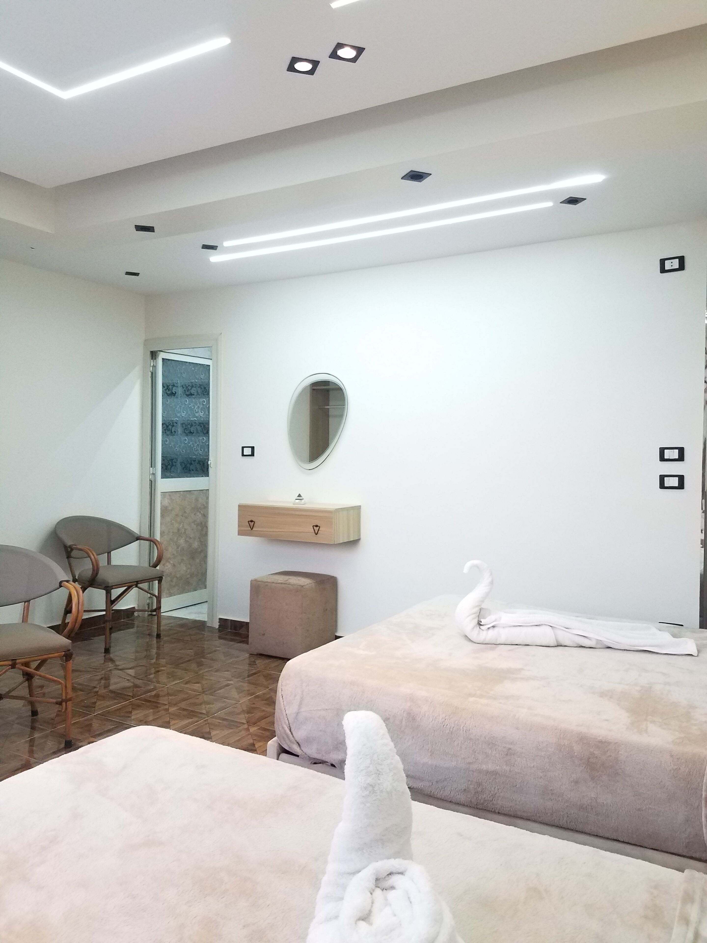 Habitación de hotel con dos camas, una mesita, una silla, un espejo y una ventana.