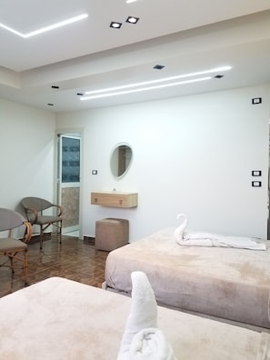 A hotel room with two beds, a small table, a chair, a mirror, and a window. - Pyramids Terrace INN (Giza)