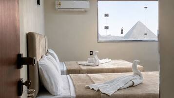 Habitación de hotel con dos camas, una ventana con vista a una pirámide, un equipo de aire acondicionado e iluminación de techo moderna.