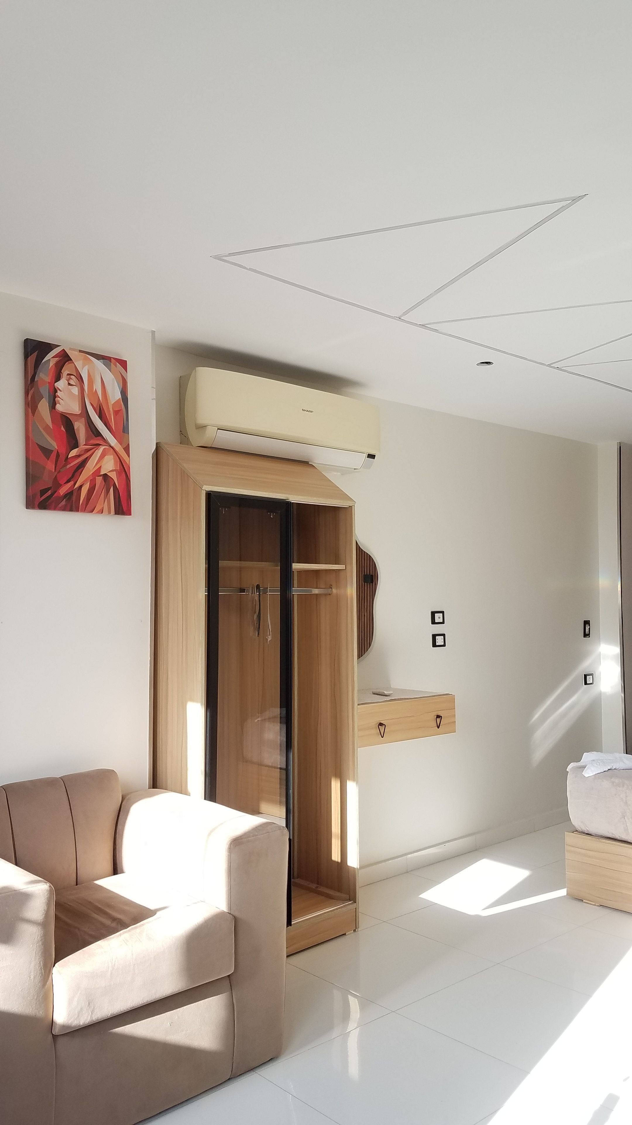 A modern room with a beige sofa, a wooden wardrobe, and a painting on the wall.