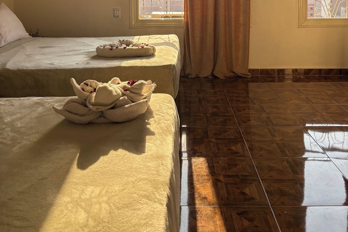 A hotel room with two beds, a large window with a view of a mountain, and a ceiling fan.