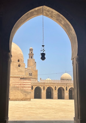 An archway leading to a courtyard with a building featuring domes and a minaret. - Pyramids Terrace INN (Giza)