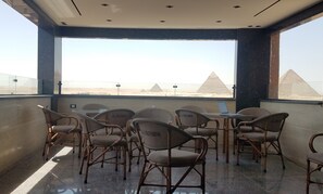 A balcony with wicker chairs and a laptop, overlooking pyramids. - Pyramids Terrace INN (Giza)